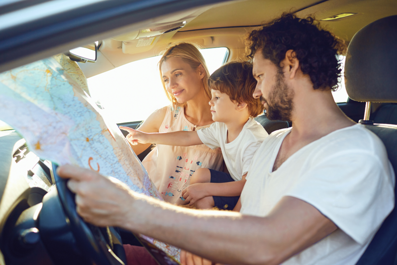 Mutter, Vater und Kind im Auto lesen eine Landkarte auf dem Weg in den Sommerurlaub