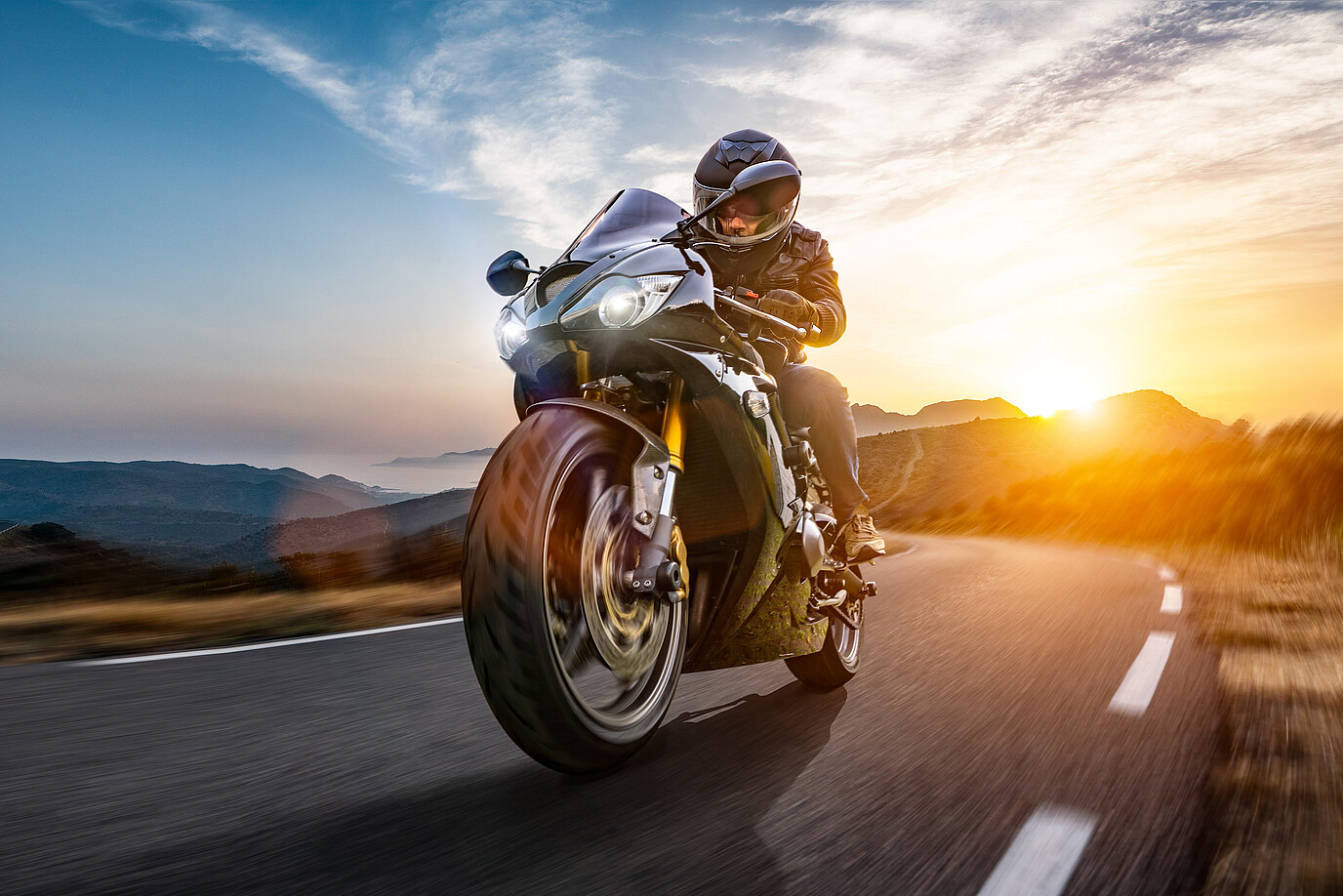 Motorradfahrer fährt auf einer Straße mit dem Sonnenuntergang im Hintergrund