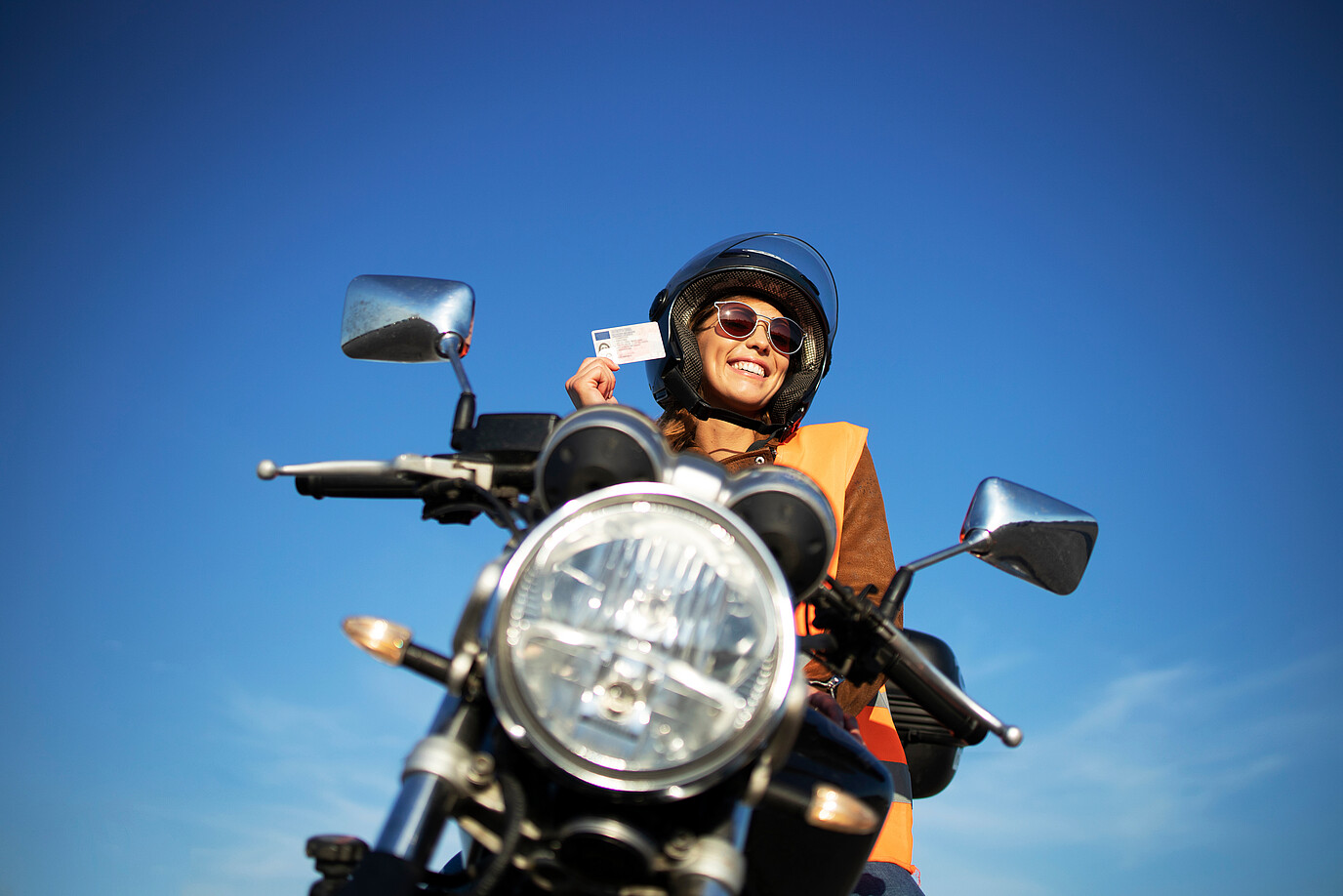 Eine Frau sitzt auf ihrem Motorrad und hält lachend ihren Führerschein in der Hand